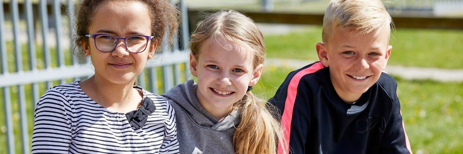 Tre børn sidder i skolegård